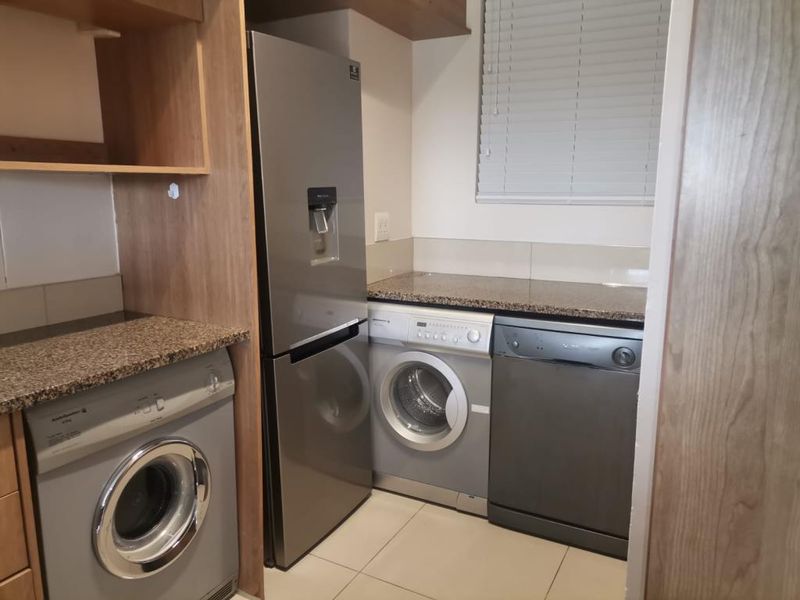 A functional scullery area featuring granite countertops, built-in cabinetry, and space for multiple appliances including a washing machine and dishwasher.