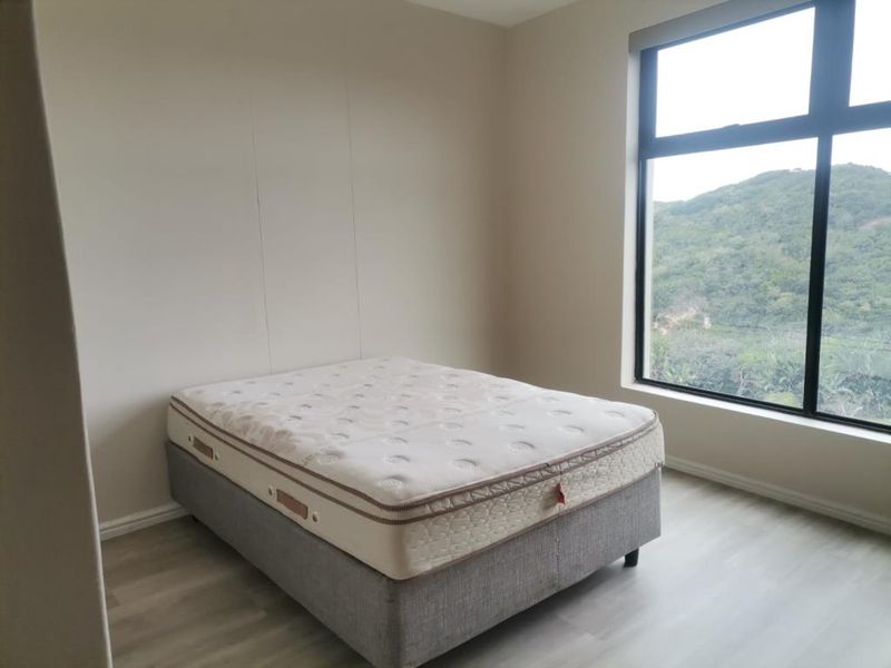 A bright bedroom featuring modern laminate flooring and a large window offering scenic hillside views.
