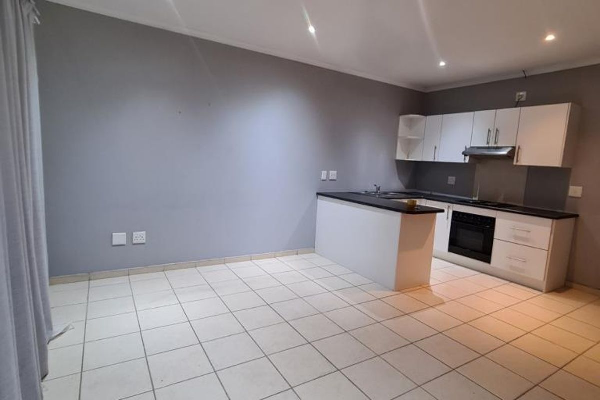 An open-plan living and kitchen area featuring tiled flooring, recessed lighting, and a modern kitchen with built-in cabinetry, oven, and hob.