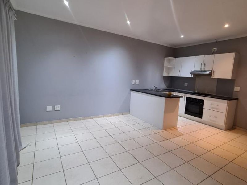 An open-plan living and kitchen area featuring tiled flooring, recessed lighting, and a modern kitchen with built-in cabinetry, oven, and hob.