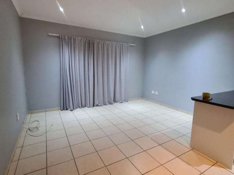 An open-plan living area featuring neutral tiled flooring, recessed downlighting, and a partial view of a kitchen counter.