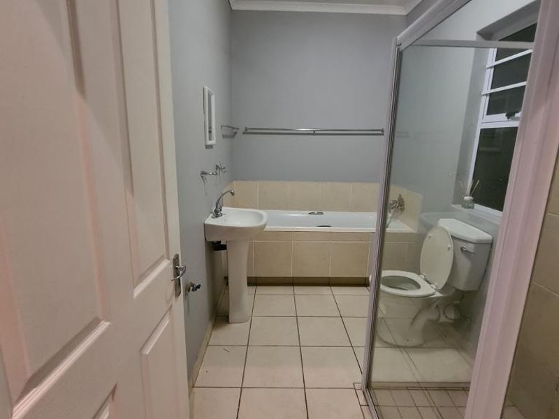 A functional bathroom featuring a pedestal basin, built-in bathtub, separate shower enclosure, and tiled flooring.