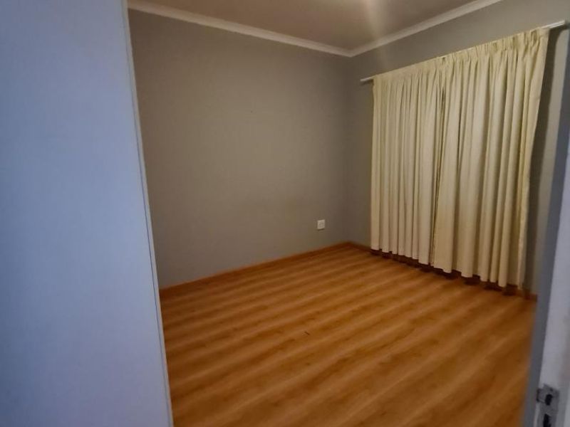 A vacant bedroom featuring laminate flooring, neutral grey walls, and a simple ceiling light fixture, offering a clean canvas for personalization.