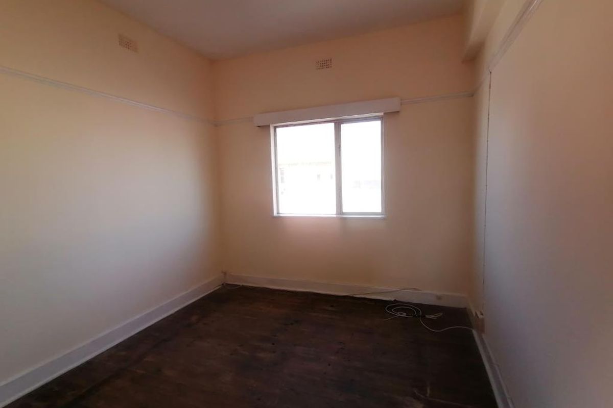 An empty bedroom featuring original timber flooring, picture rails, and a sliding window, offering a blank canvas for renovation or interior design.
