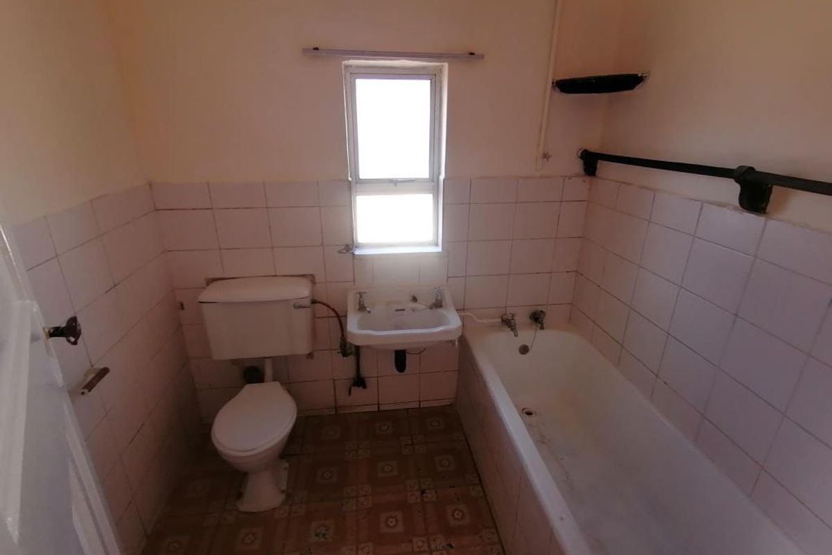A dated bathroom featuring a standard bathtub, toilet, and wall-mounted basin with tiled finishes, requiring renovation to modernize the space.