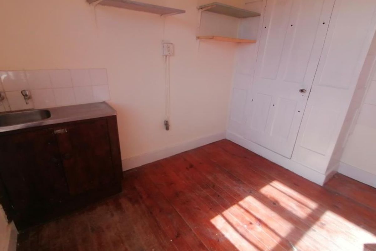 A compact kitchen area featuring original timber flooring, a stainless steel sink with tiled splashback, and built-in storage cupboards.