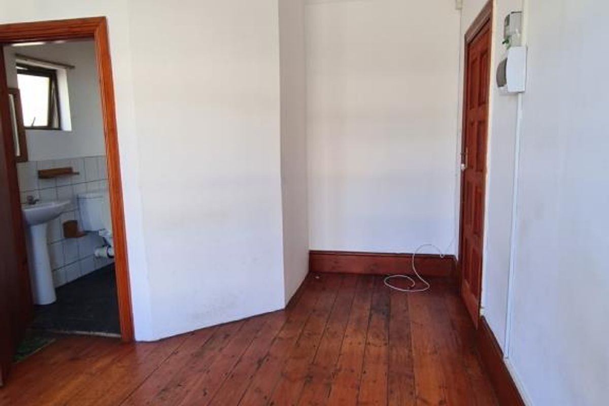 An empty bedroom featuring original timber flooring, classic cornice detailing, and a solid timber door, leading into an adjacent bathroom.