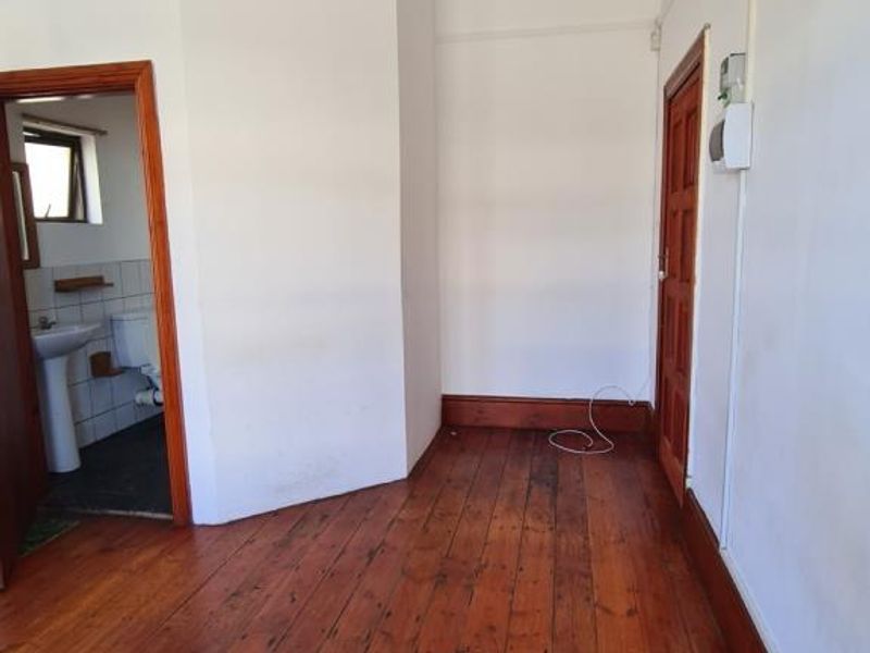 An empty bedroom featuring original timber flooring, classic cornice detailing, and a solid timber door, leading into an adjacent bathroom.