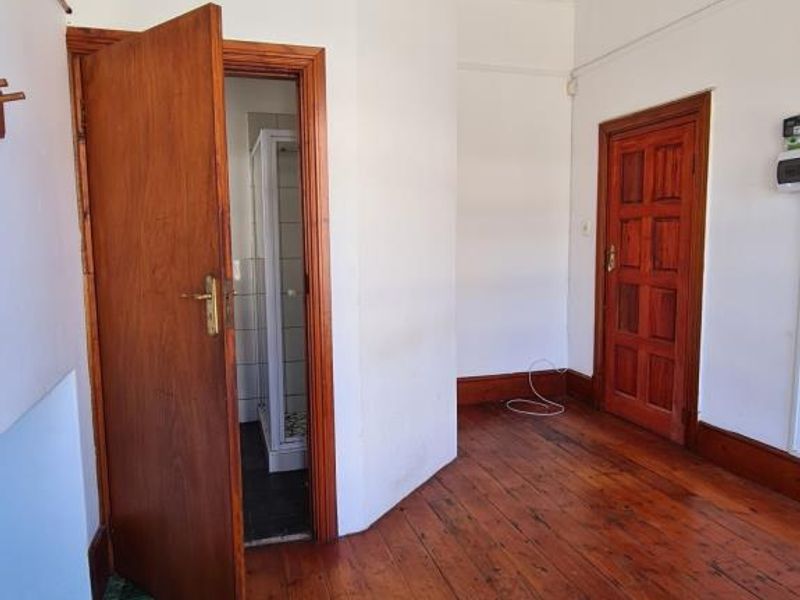 A vacant hallway featuring original timber flooring, traditional timber doors, and decorative cornice detailing, leading to an adjacent bathroom area.
