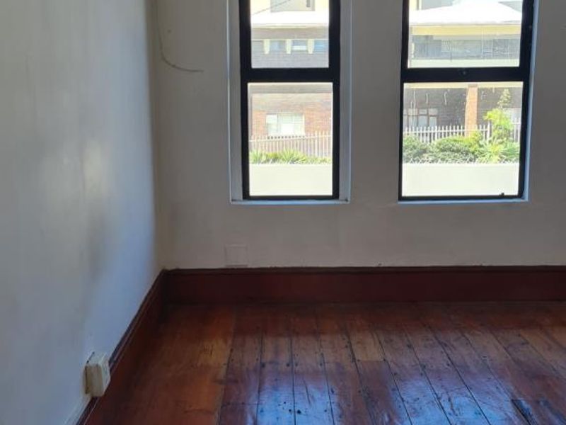 An empty bedroom featuring original timber flooring, large casement windows, and wall-mounted lighting, requiring cosmetic updates to the walls and floors.