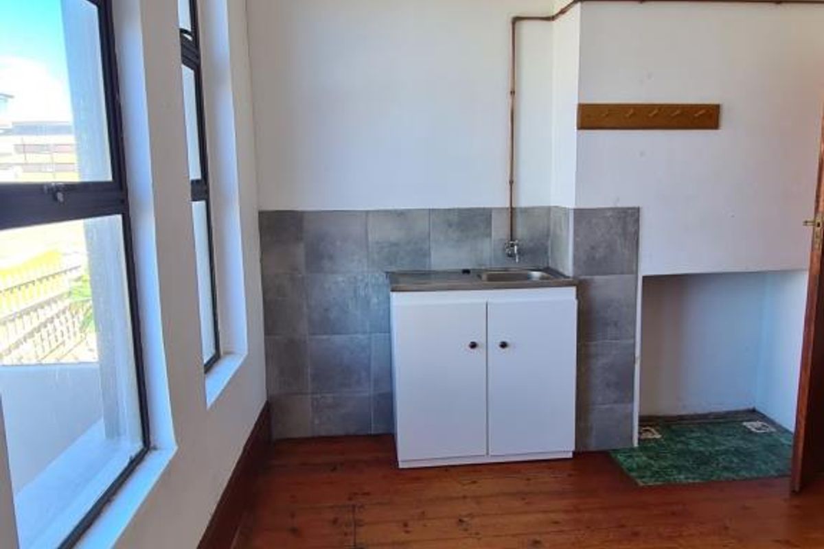 A compact kitchen area featuring timber flooring, a small sink unit with tiled splashback, and exposed copper piping.