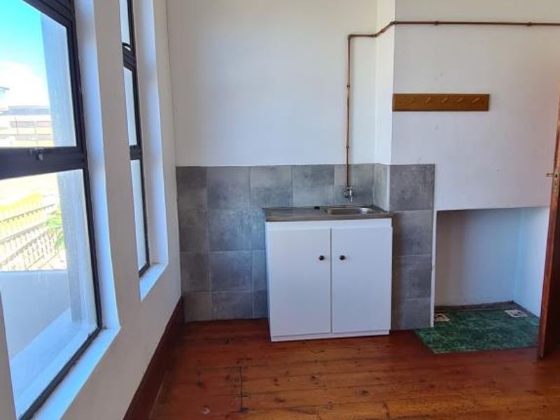 A compact kitchen area featuring timber flooring, a small sink unit with tiled splashback, and exposed copper piping.