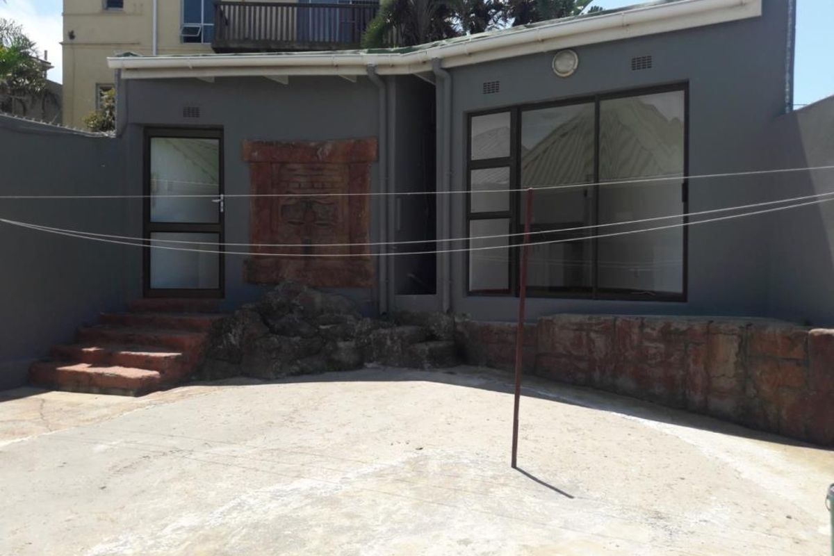 Rear exterior view of the apartment featuring a concrete patio area, stone feature wall, and sliding glass door access.