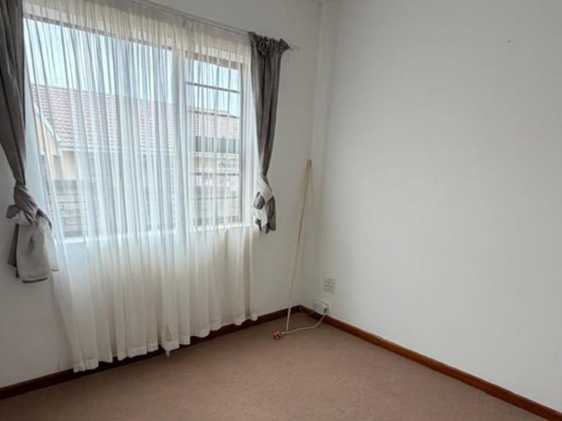 A clean, empty bedroom featuring neutral carpet flooring, a window with curtains, and standard electrical fixtures.