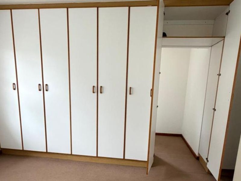 A bedroom featuring extensive built-in cupboards and carpeted flooring, offering ample storage space in a neutral setting.