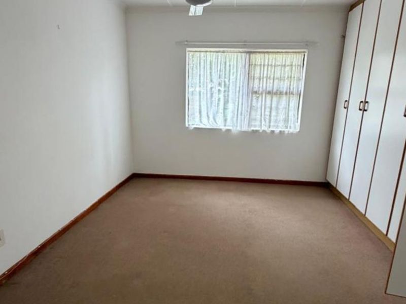 An empty bedroom featuring built-in cupboards, carpeted flooring, and a window, offering a blank canvas for personalization.