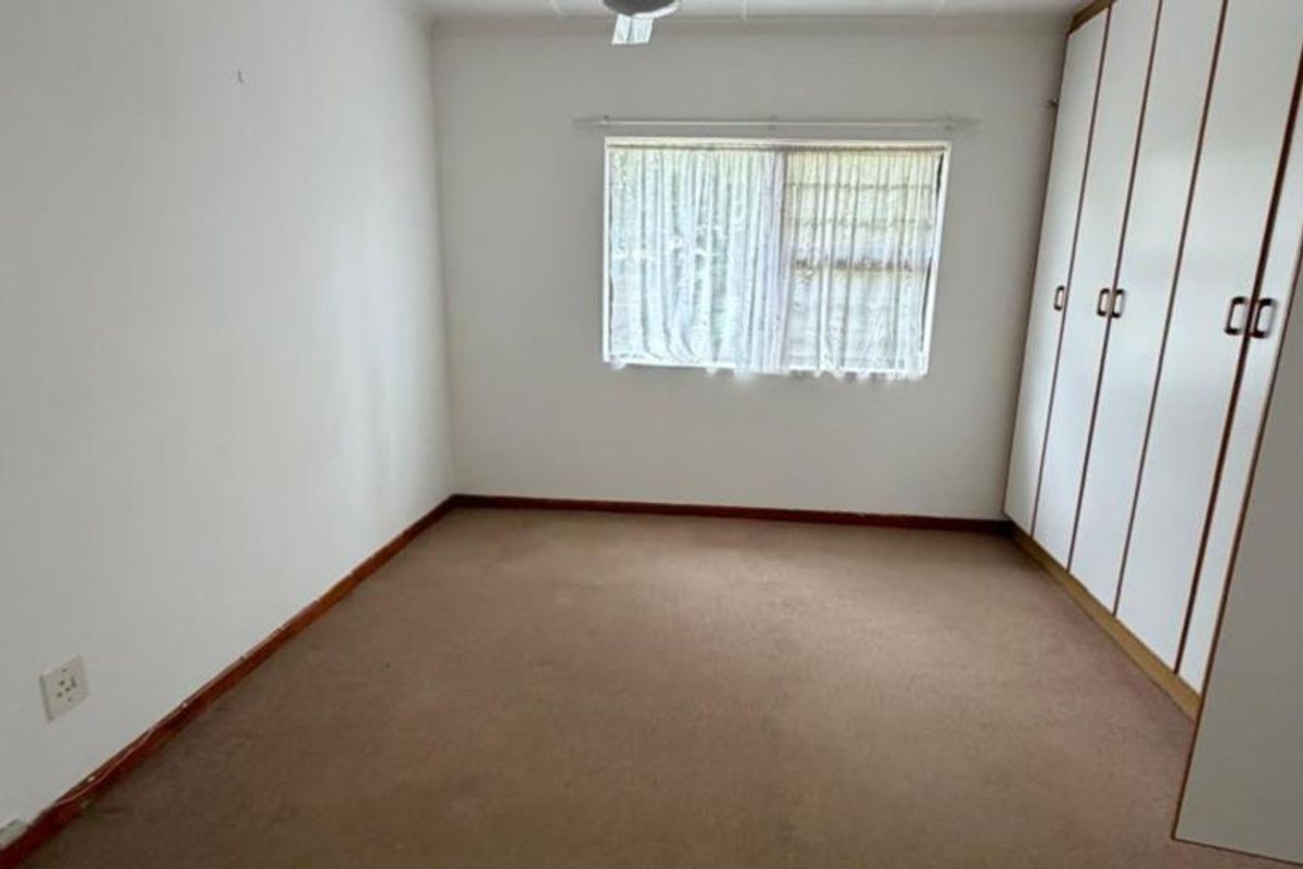 An empty bedroom featuring built-in cupboards, carpeted flooring, and a window, offering a blank canvas for personalization.