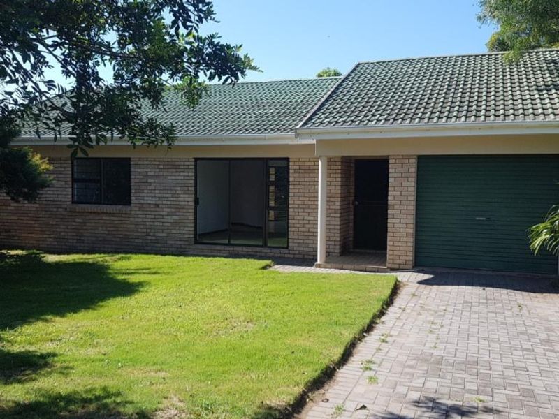 Front view of a single-story brick house featuring a tiled roof, integrated garage, paved driveway, and a small front lawn.