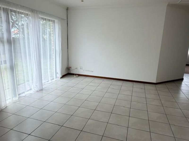 A bright, empty living room featuring neutral tiled flooring and a large sliding glass door providing access to the garden area.