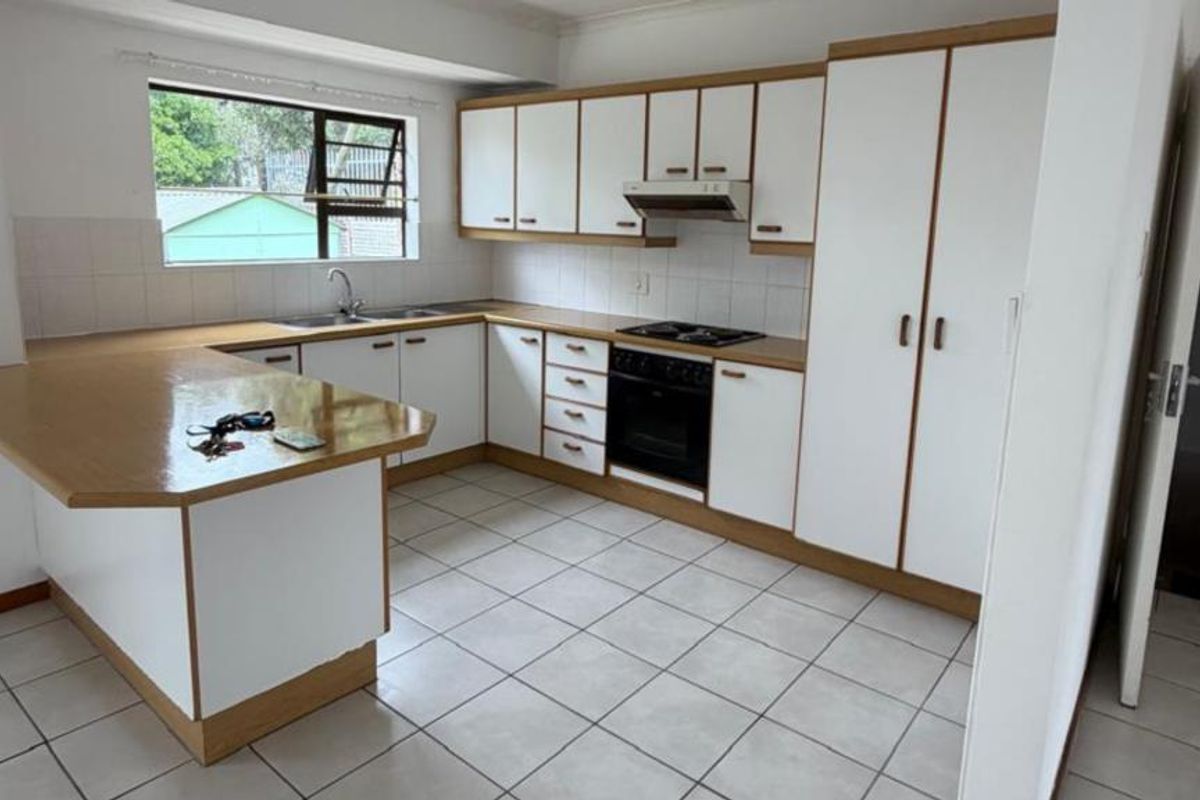 A functional kitchen featuring white cabinetry with wood trim, laminate countertops, built-in oven, hob, extractor fan, and tiled flooring.