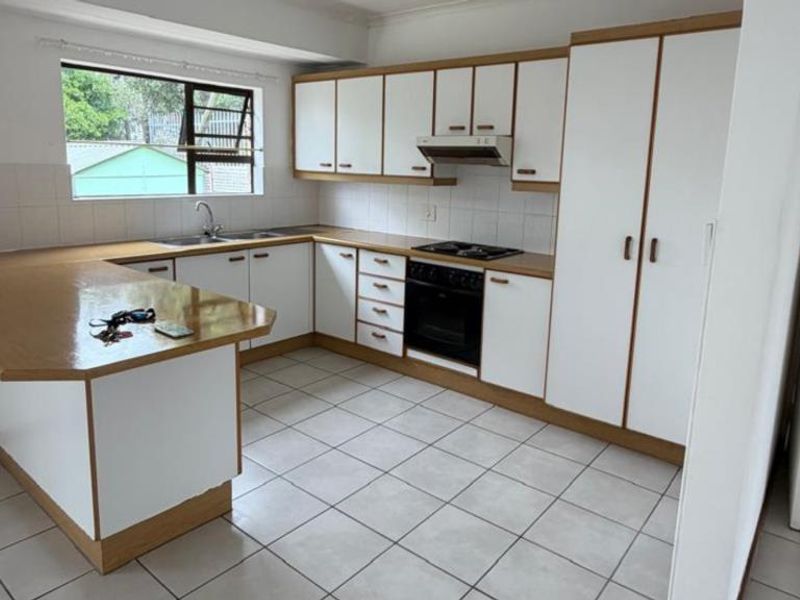 A functional kitchen featuring white cabinetry with wood trim, laminate countertops, built-in oven, hob, extractor fan, and tiled flooring.