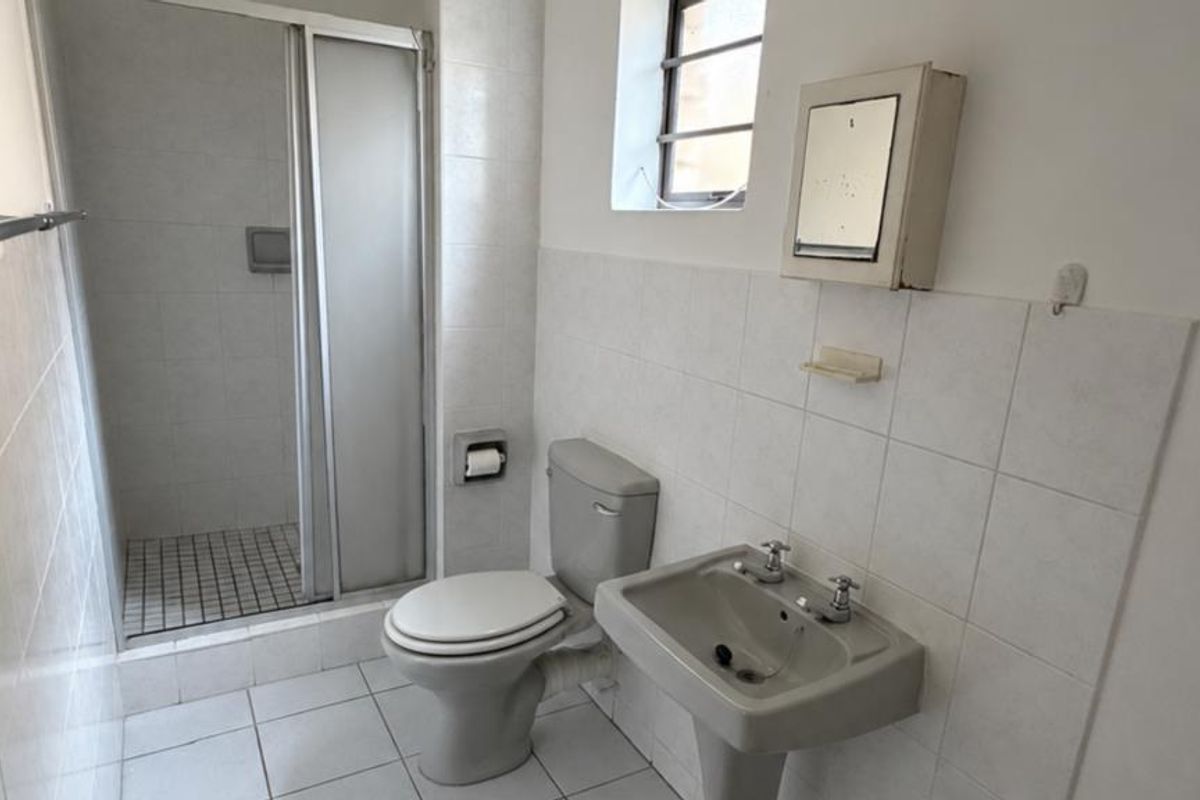 A functional bathroom featuring a shower enclosure, pedestal basin, and toilet with neutral wall and floor tiling.