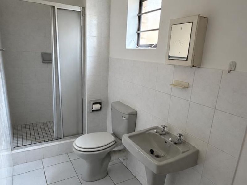A functional bathroom featuring a shower enclosure, pedestal basin, and toilet with neutral wall and floor tiling.