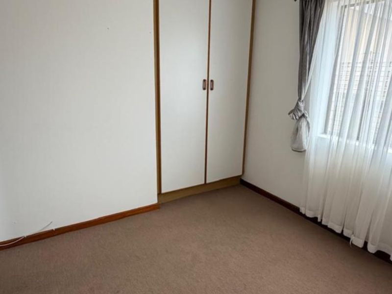 A vacant bedroom featuring built-in wardrobes, carpeted flooring, and neutral wall finishes, offering a blank canvas for potential updates.