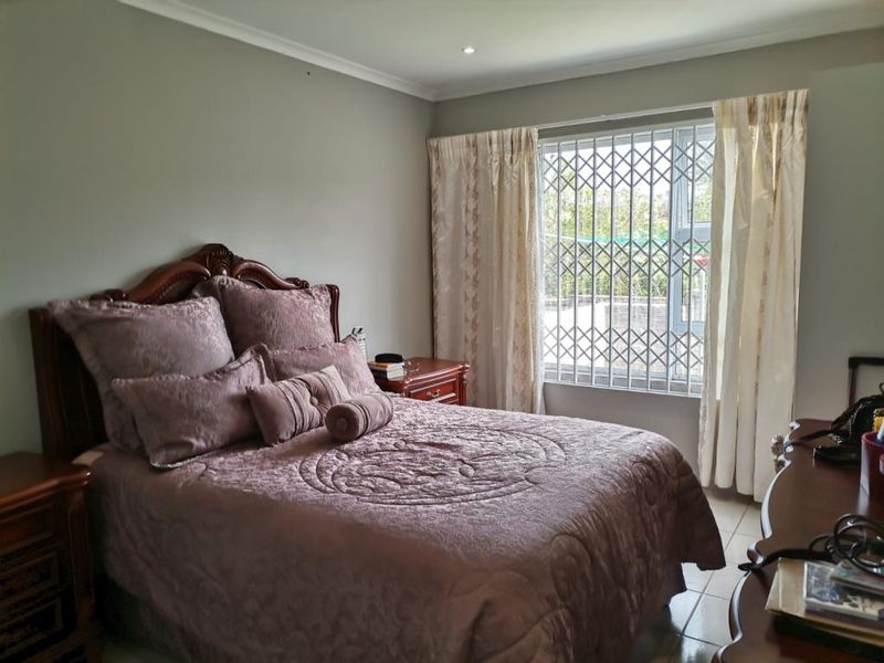 A well-maintained bedroom featuring tiled flooring, cove cornicing, and a window fitted with a security gate for added peace of mind.