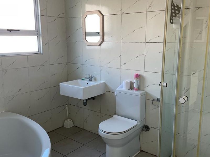 A functional bathroom featuring a wall-mounted basin, toilet, shower enclosure, and a bathtub with tiled finishes throughout.