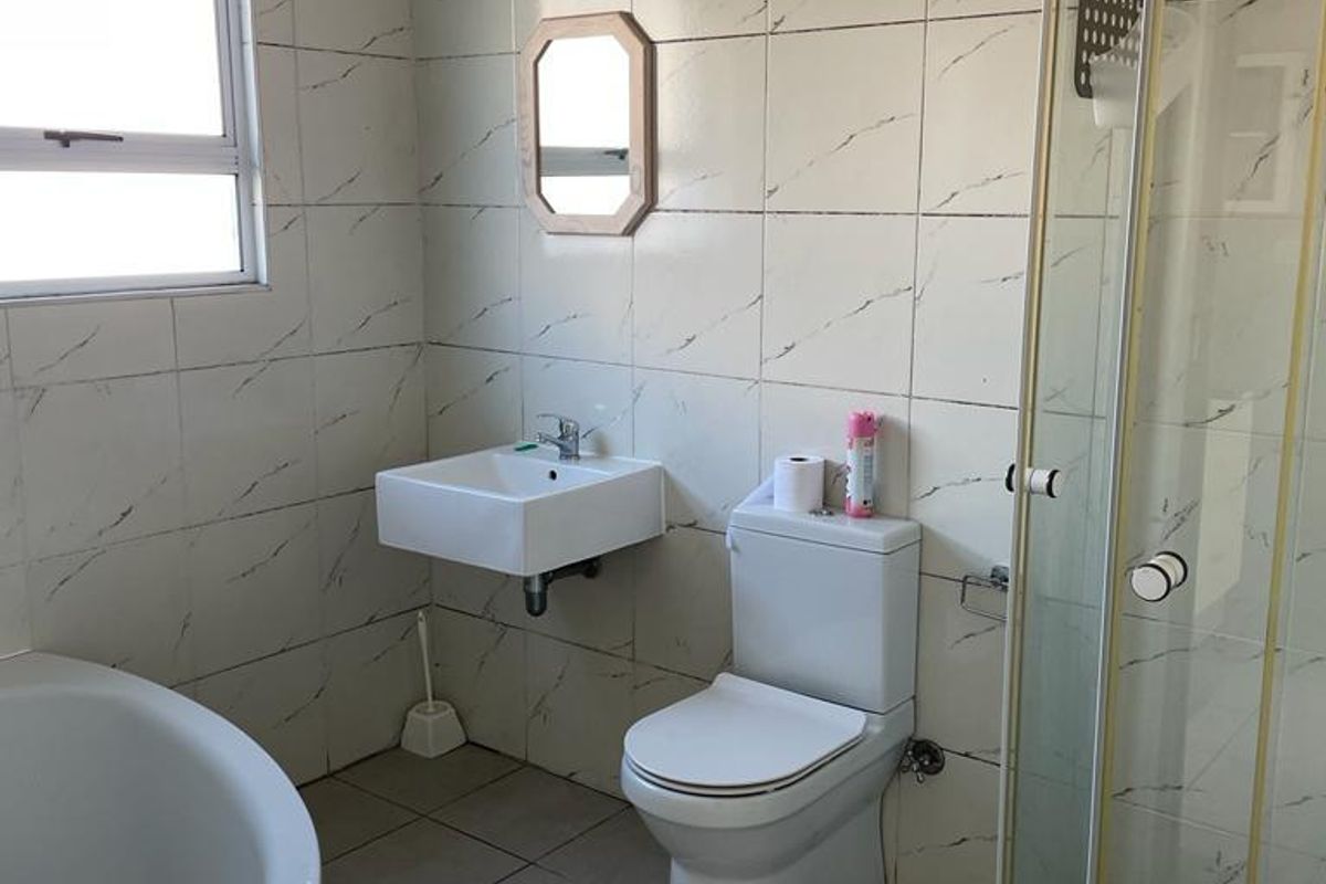 A functional bathroom featuring a wall-mounted basin, toilet, shower enclosure, and a bathtub with tiled finishes throughout.