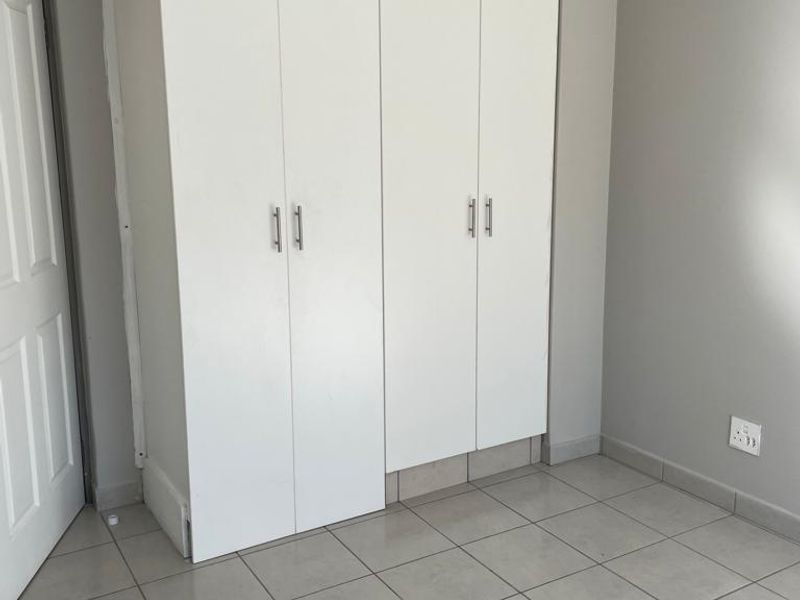 A bedroom featuring neutral grey walls, tiled flooring, and white built-in cupboards with modern handles.