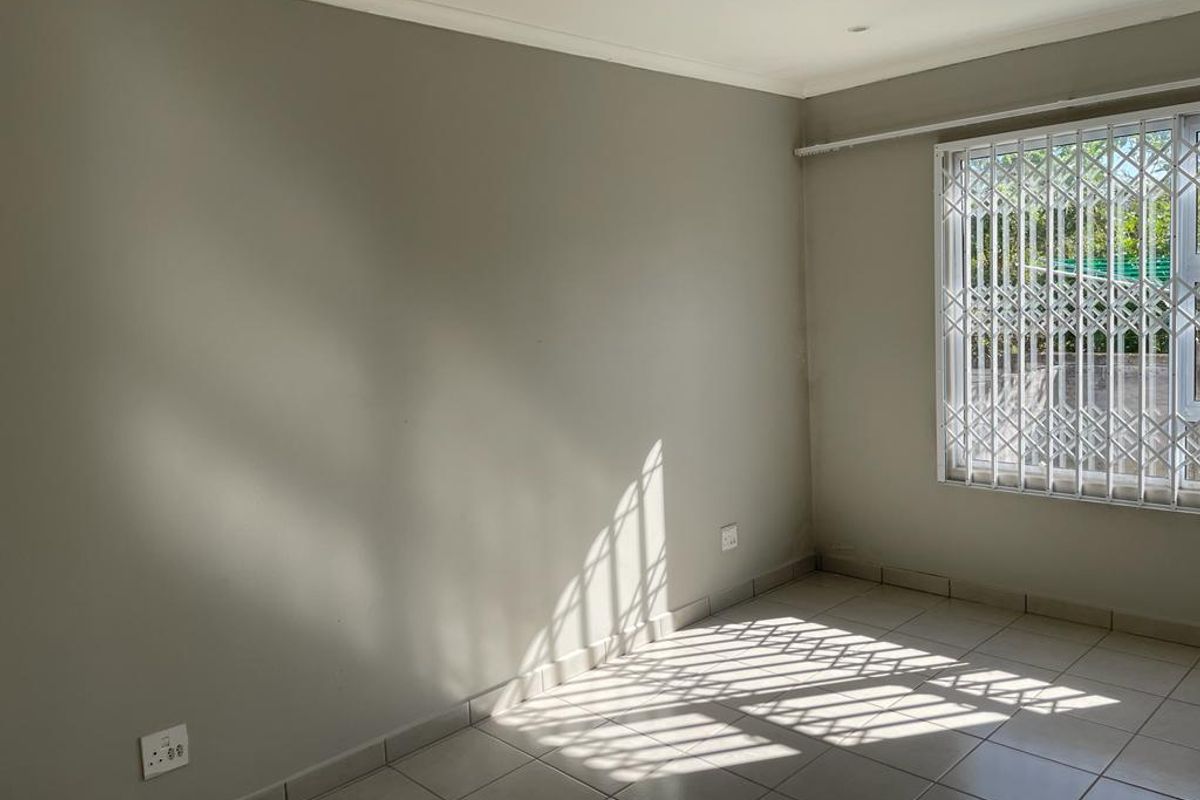 A bright, empty bedroom featuring neutral wall paint, tiled flooring, and a window fitted with a security gate.