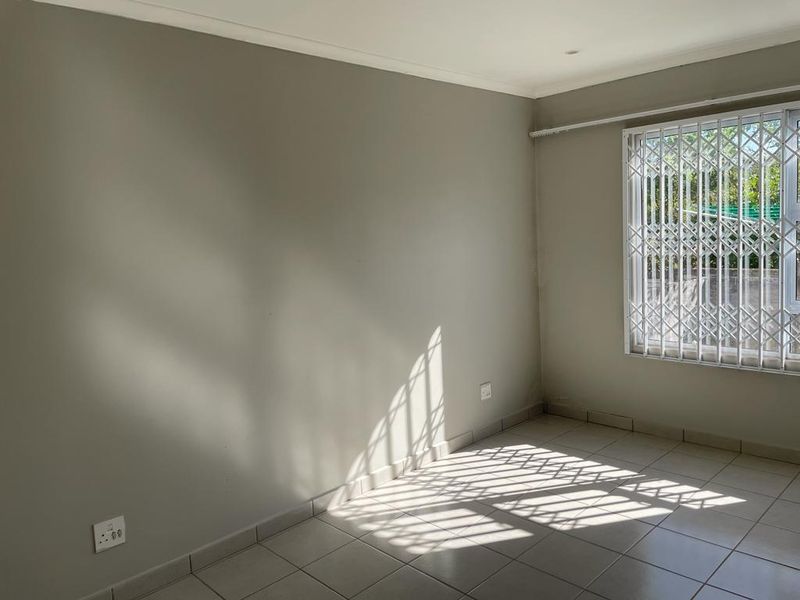 A bright, empty bedroom featuring neutral wall paint, tiled flooring, and a window fitted with a security gate.