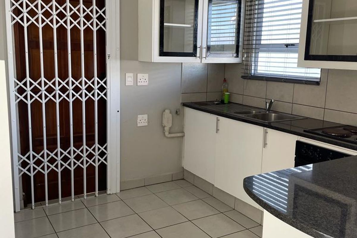A functional kitchen featuring white cabinetry, dark countertops, tiled flooring, and a security gate leading to an exterior entrance.