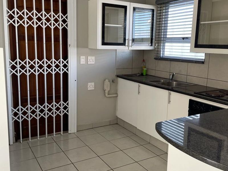 A functional kitchen featuring white cabinetry, dark countertops, tiled flooring, and a security gate leading to an exterior entrance.