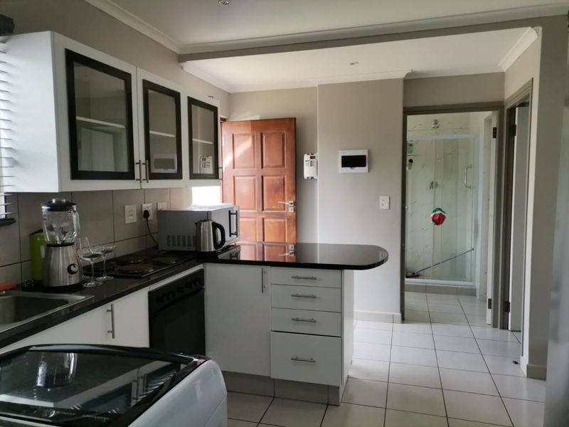 A functional kitchen featuring white cabinetry, dark granite countertops, built-in oven and hob, and tiled flooring, with direct access to an adjacent bathroom.