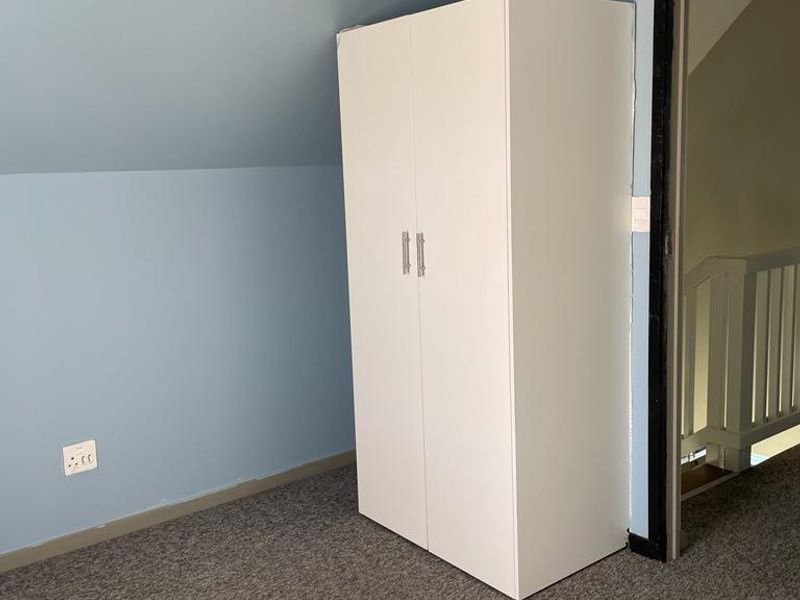 A bedroom featuring a sloped ceiling, carpeted flooring, and a white built-in wardrobe, offering a clean and neutral space ready for personalization.