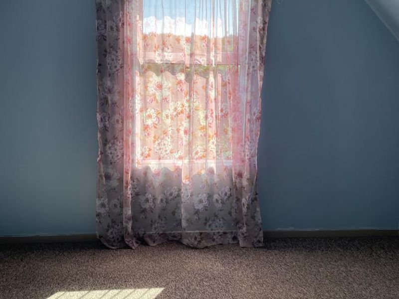 An empty bedroom featuring a sloped ceiling, carpeted flooring, and a single window with natural light.
