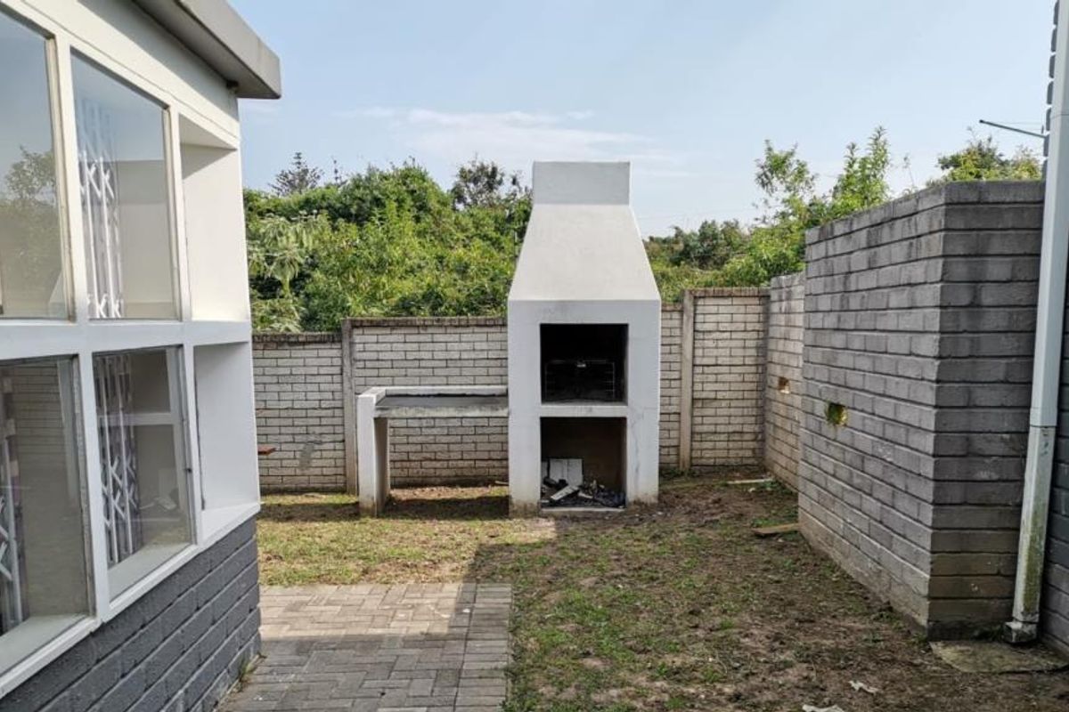 Rear garden area featuring a built-in braai, paved patio section, and perimeter brick walling, offering potential for outdoor entertainment space development.