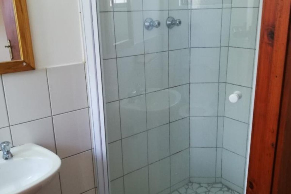 A functional bathroom featuring a pedestal basin and a corner shower enclosure with tiled walls and a mosaic floor.