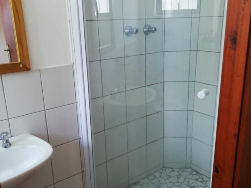 A functional bathroom featuring a pedestal basin and a corner shower enclosure with tiled walls and a mosaic floor.