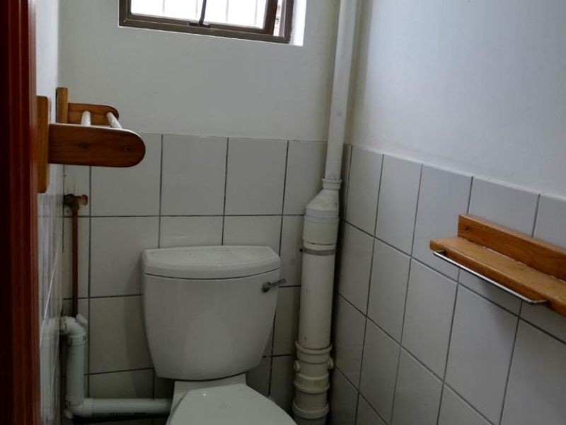 A compact bathroom featuring a standard toilet, washbasin, and tiled walls with exposed plumbing fixtures.