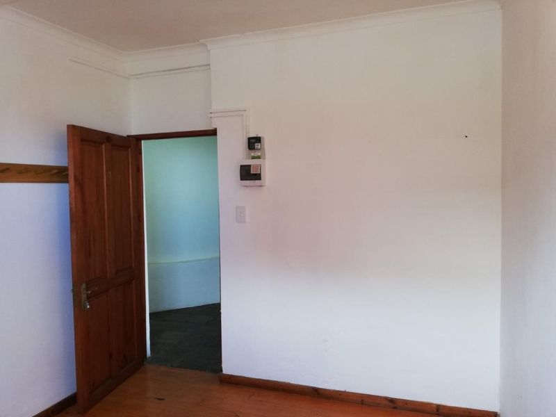 A vacant hallway featuring timber flooring, wooden door, and skirting boards, with an exposed electrical distribution board mounted on the wall.