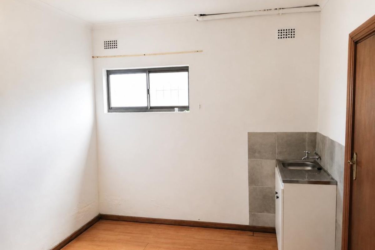 A compact, empty utility or scullery area featuring a stainless steel sink, tiled splashback, and laminate flooring, ready for functional updates.