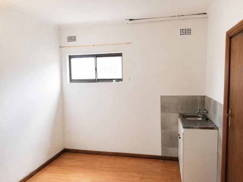 A compact, empty utility or scullery area featuring a stainless steel sink, tiled splashback, and laminate flooring, ready for functional updates.