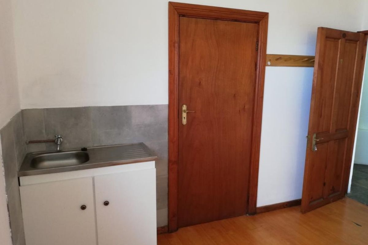 A functional utility area featuring a stainless steel sink, tiled splashback, and timber doors, providing a practical space for laundry or secondary storage needs.