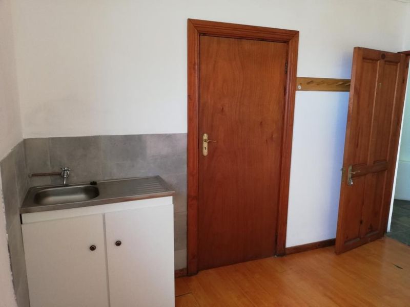 A functional utility area featuring a stainless steel sink, tiled splashback, and timber doors, providing a practical space for laundry or secondary storage needs.