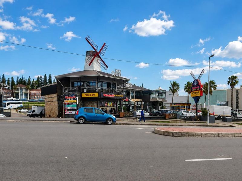 A street-level view of a commercial property featuring a prominent windmill structure and various retail signage.