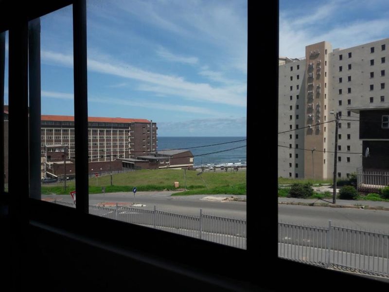 A view from an interior window looking out over a street, open land, and the ocean in the distance.